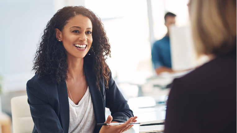 a business woman sitting at a desk having a meeting with another woman whose back is to the camera