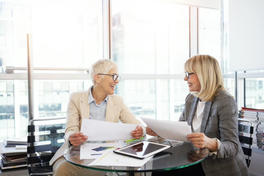 Two mature business women seated at a table looking over papers